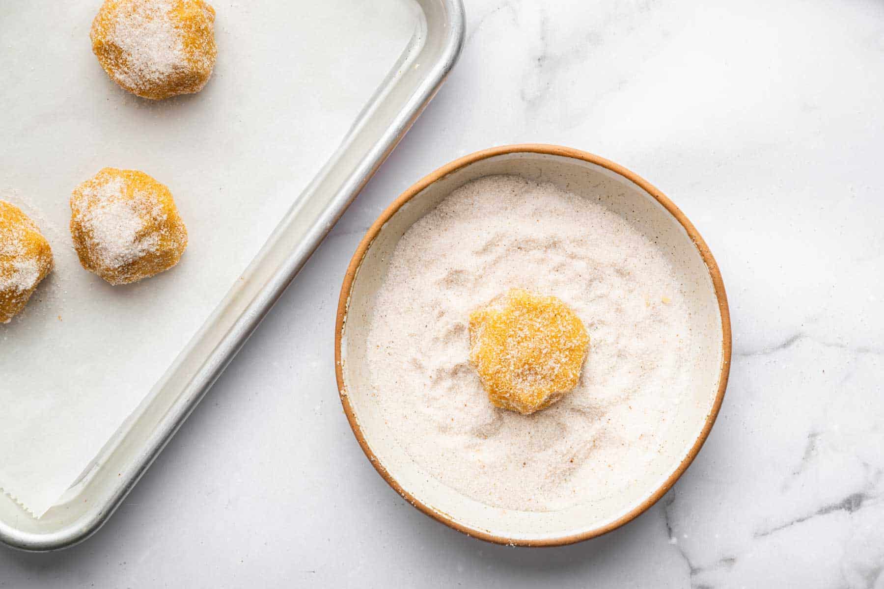 Raw dough balls being rolled in sugar before baking.