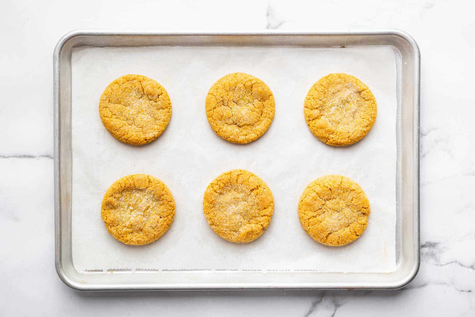 Six pumpkin sugar cookies on a parchment lined baking sheet.