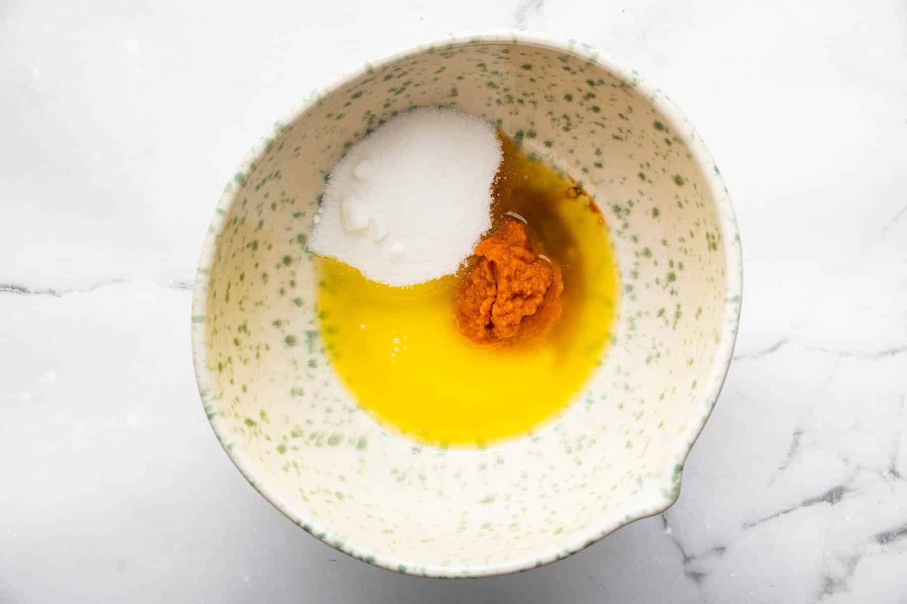 Speckled bowl with melted butter, orange batter, and sugar in it.