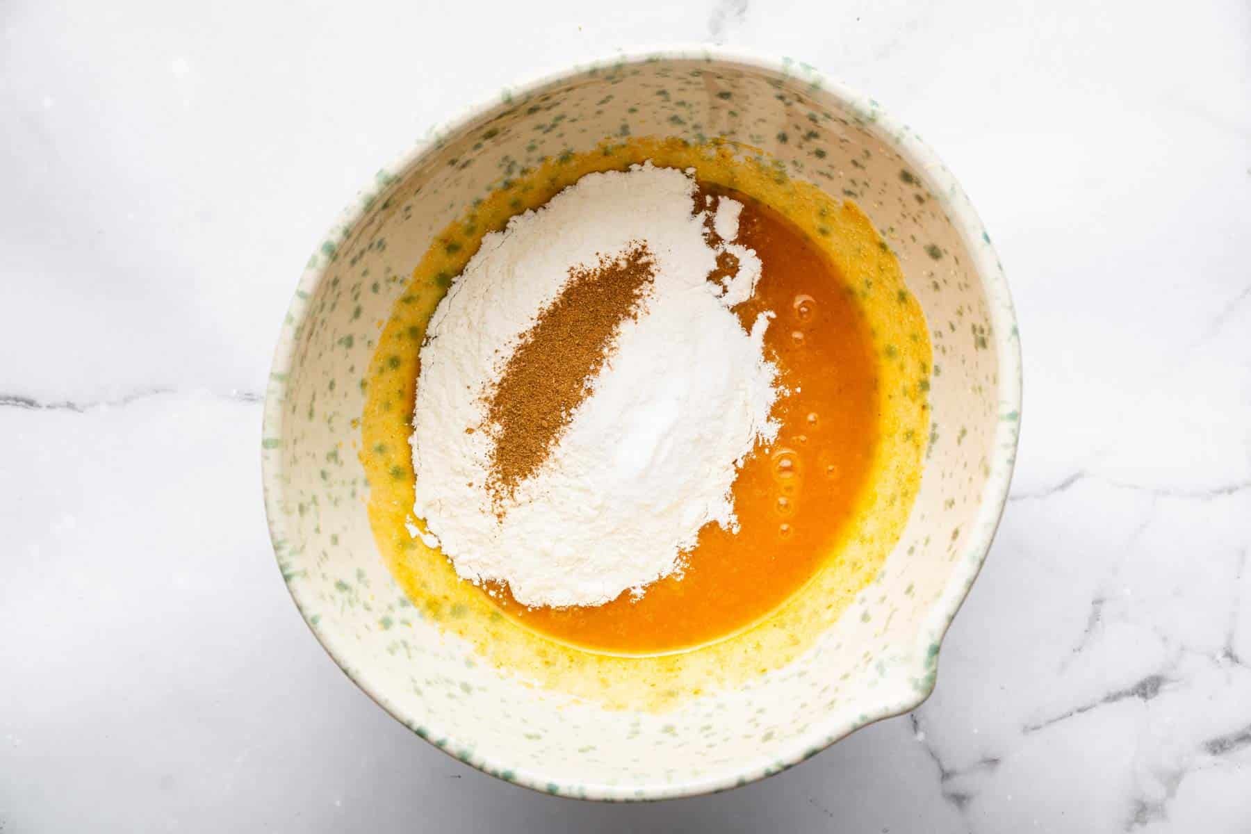 Bowl with orange batter and white and brown powder sprinkled on top.