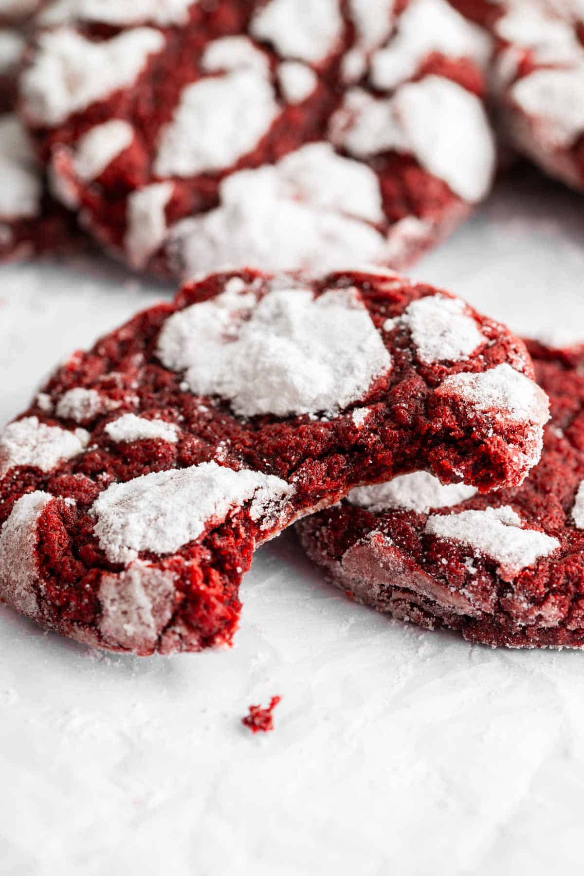 Red velvet crinkle cookies with a bite missing from one leaning on another one.