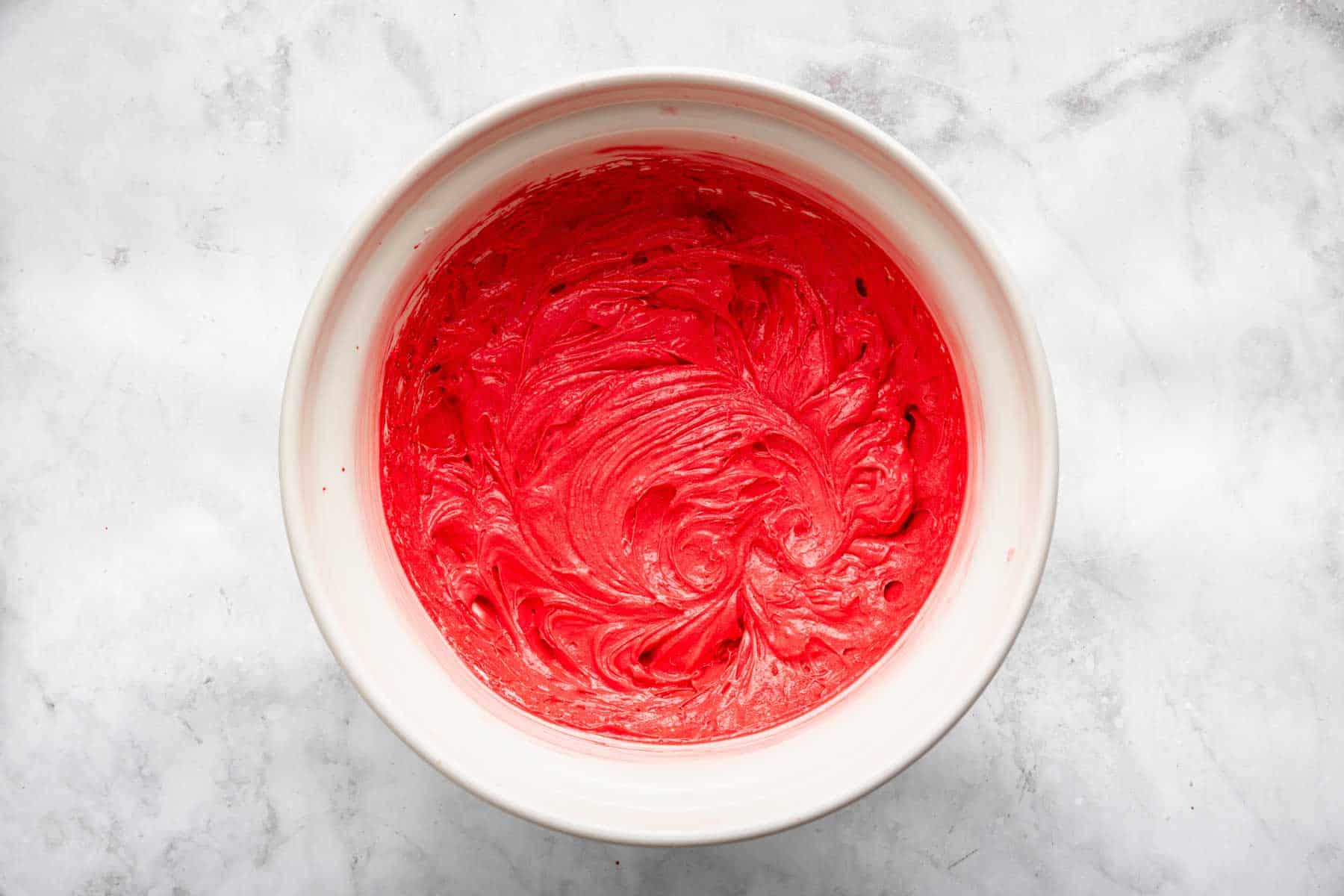 Bright red dough in a white bowl with beater swirls in it.