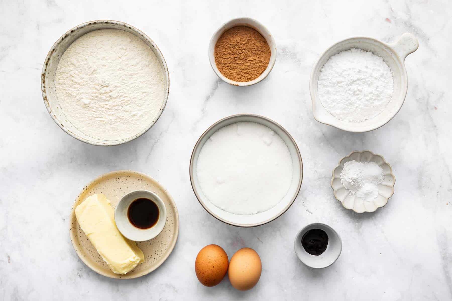 Bowl of white flour, white sugar, cocoa powder, and two eggs on a marble surface.