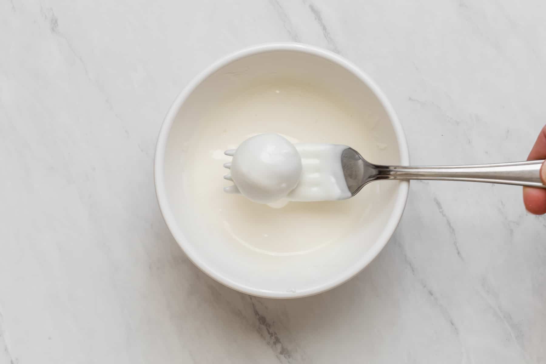 Dipping truffles in melted white chocolate with a fork.