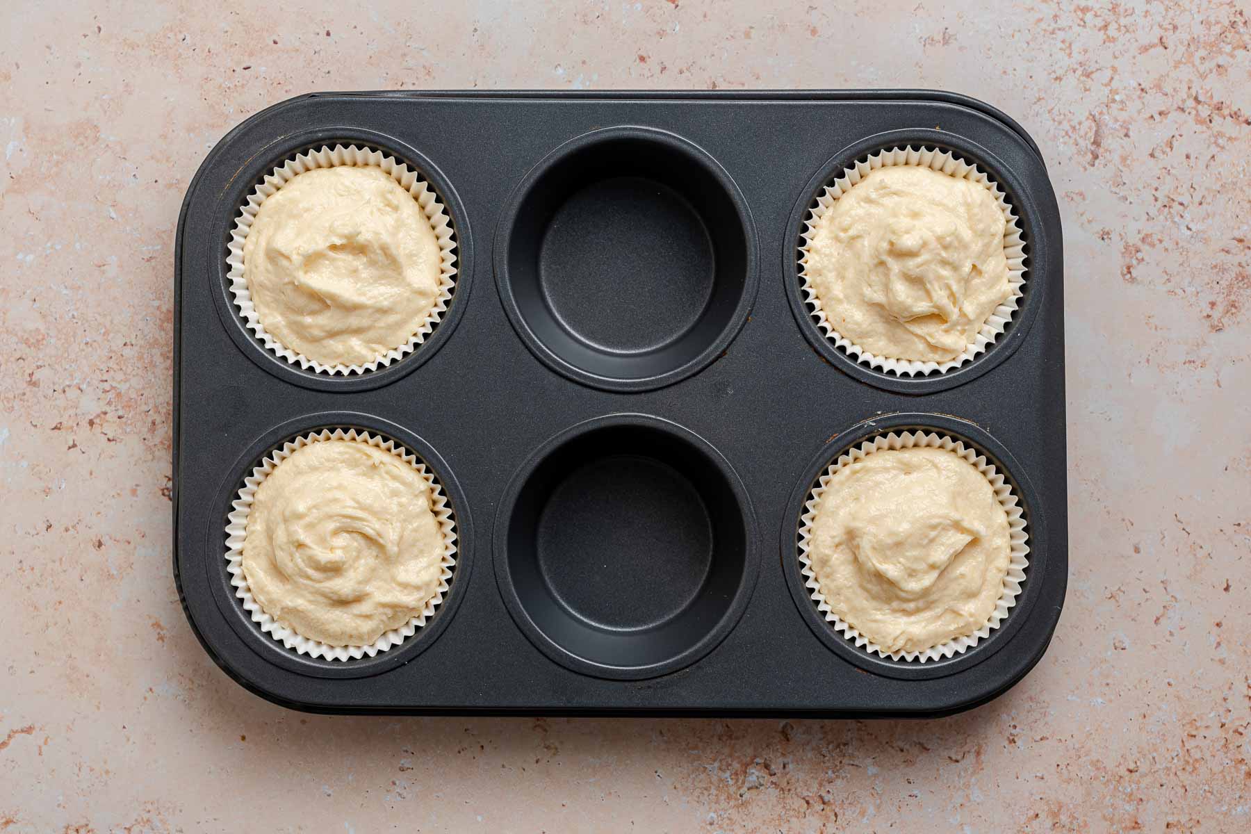 Four cupcake liners full of raw batter in muffin pan.