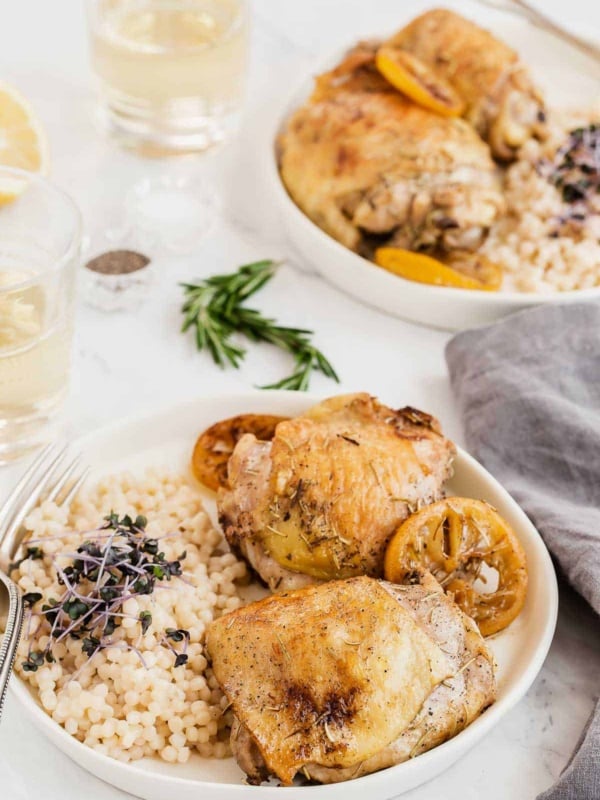 two plates of chicken thighs with lemon slices and rosemary