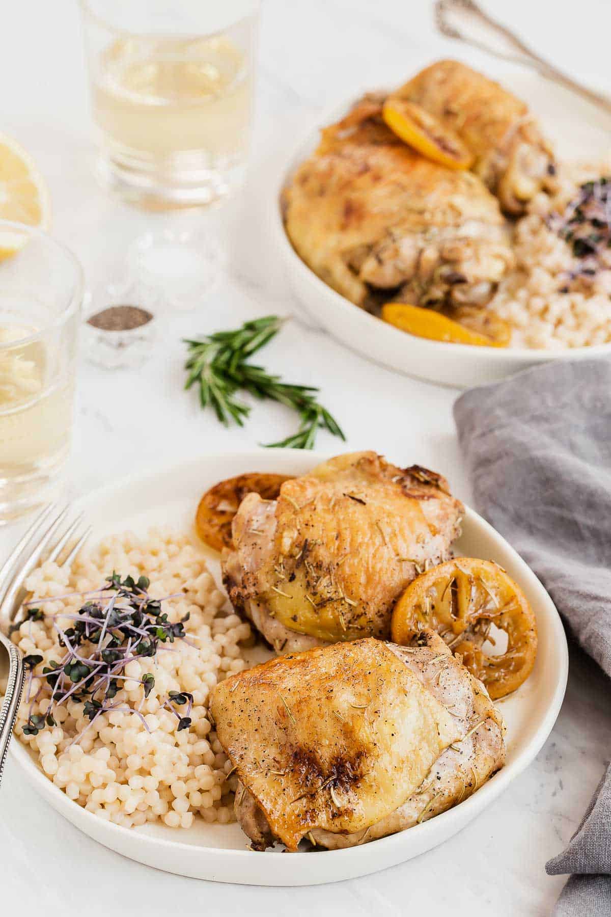 two plates of chicken thighs with lemon slices and rosemary