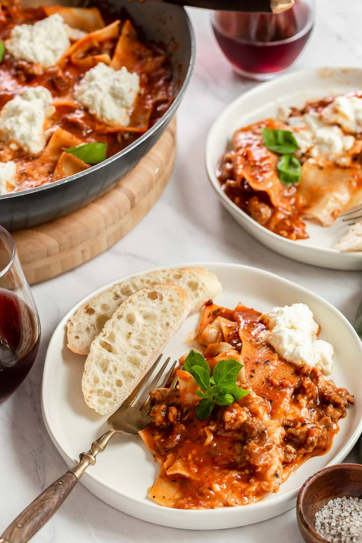 Two white plates with lasagna and skillet in background.