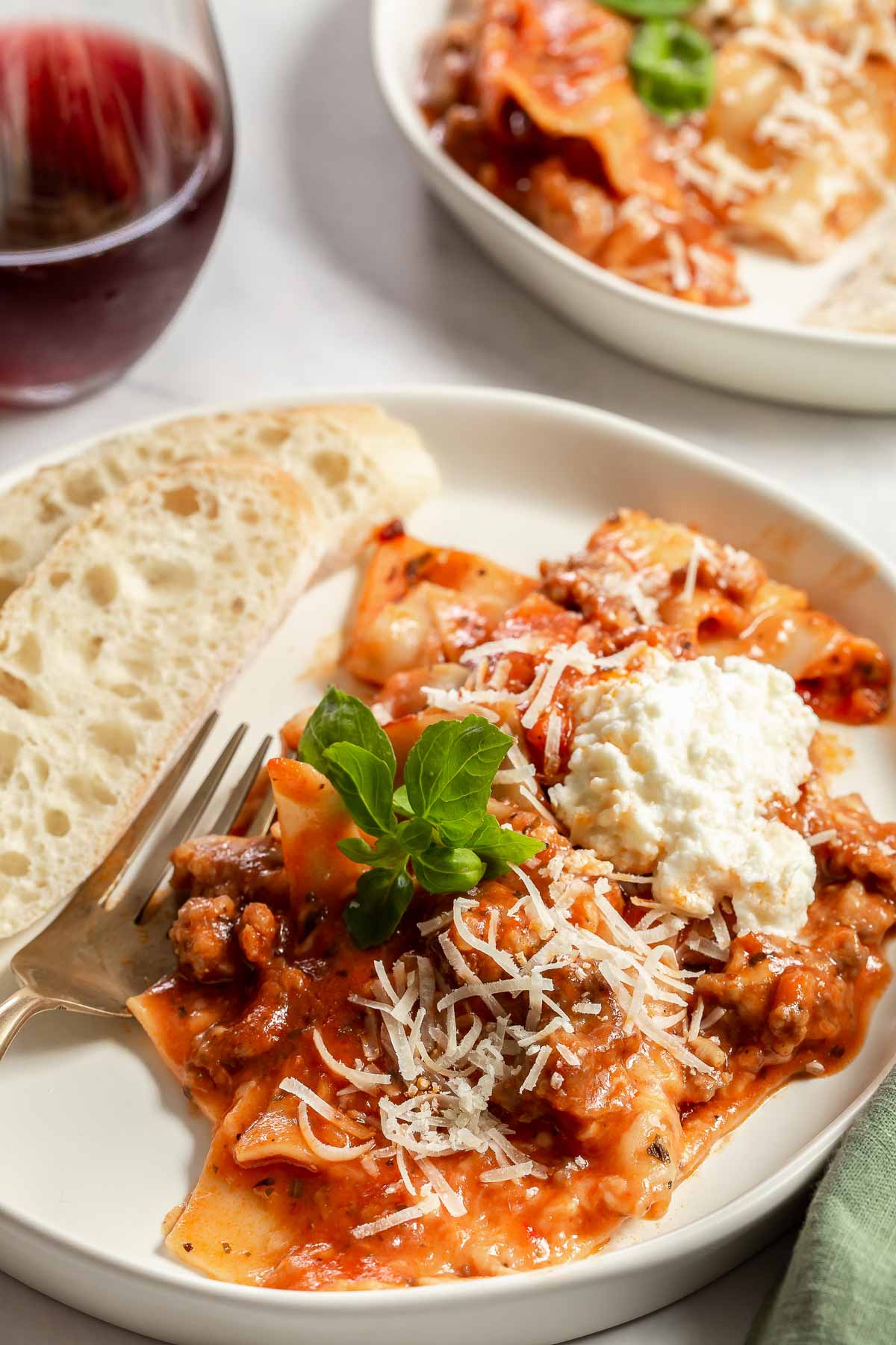 Serving of lasagna on white plate with bread.