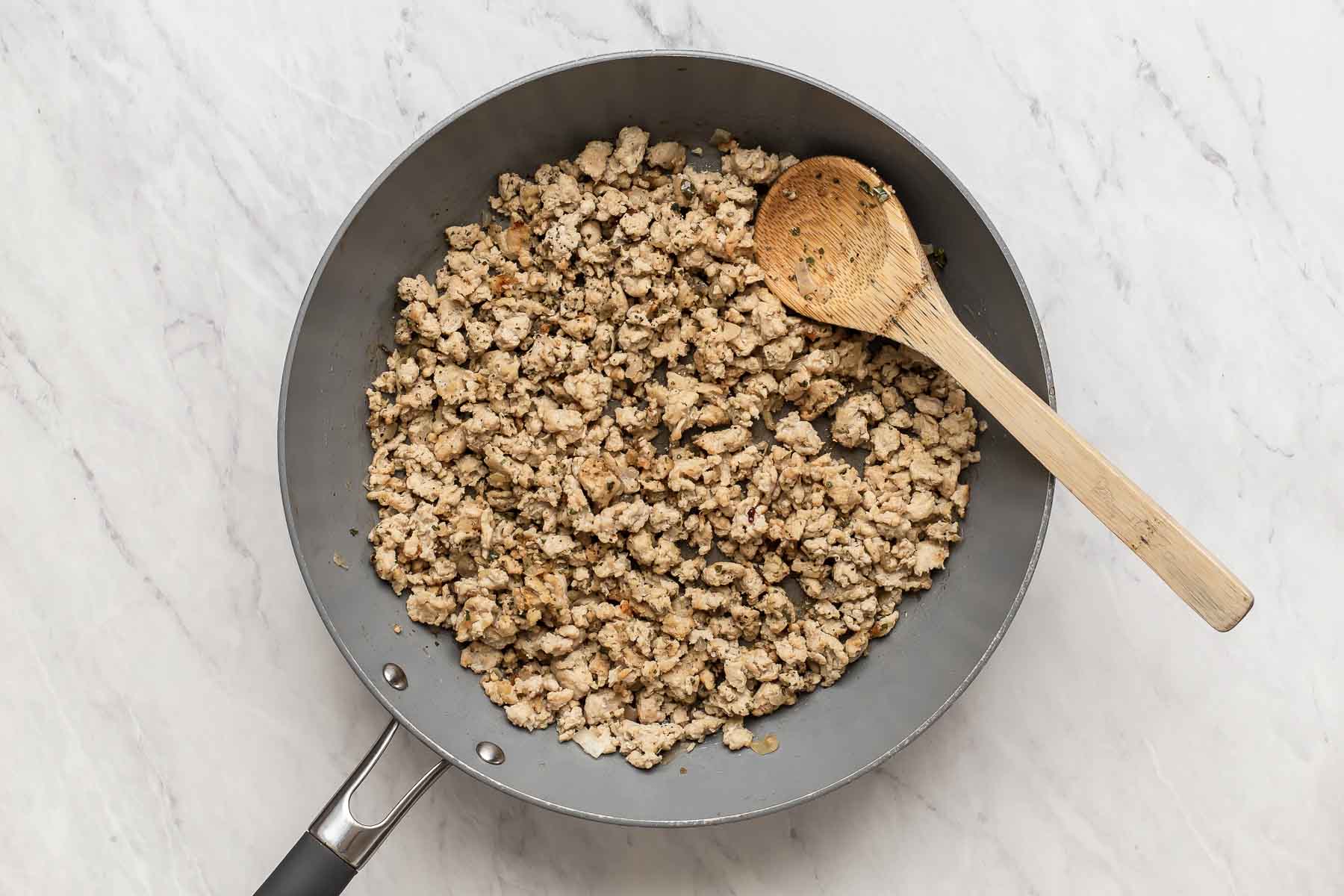 Ground chicken cooking in a skillet with wooden spoon.