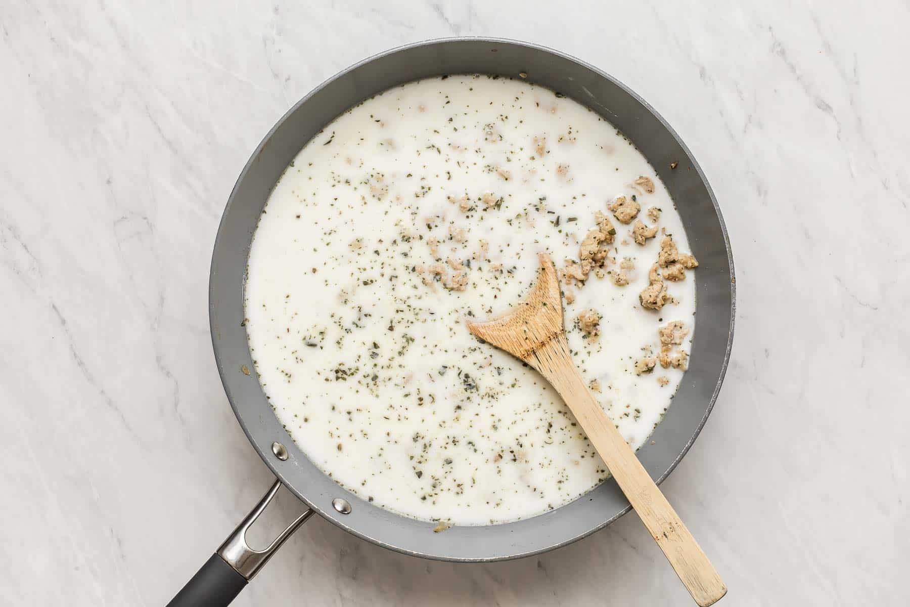 Making bรฉchamel white sauce in a skillet with a wooden spoon.