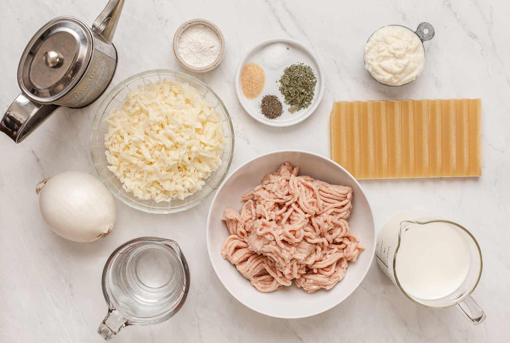Ingredients for white chicken lasagna skillet on white table.