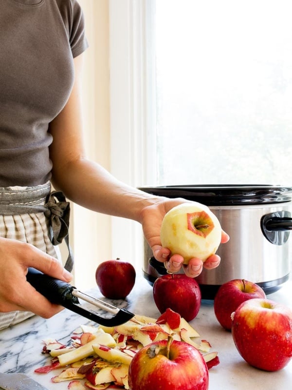 Woman peeling apples next to a slow cooker.