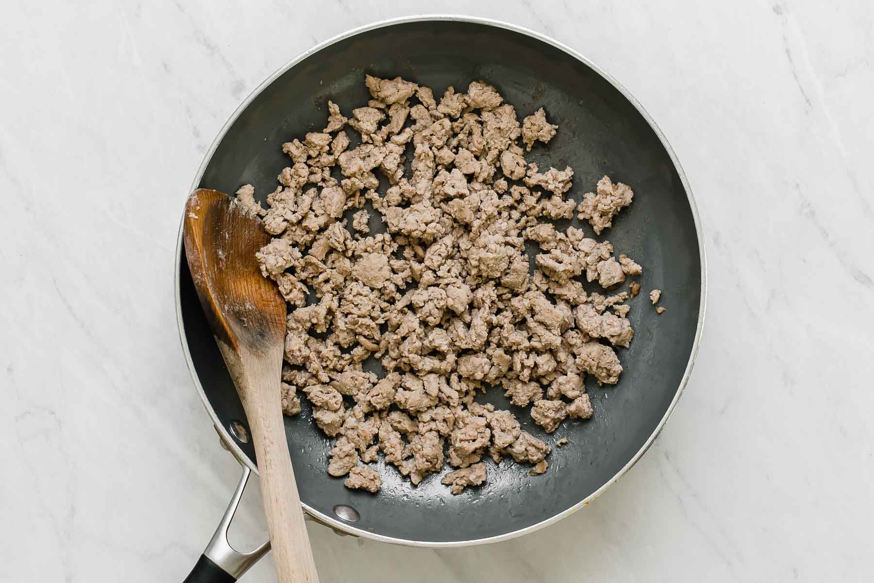 Browning ground turkey meat in a skillet with a wooden spoon.