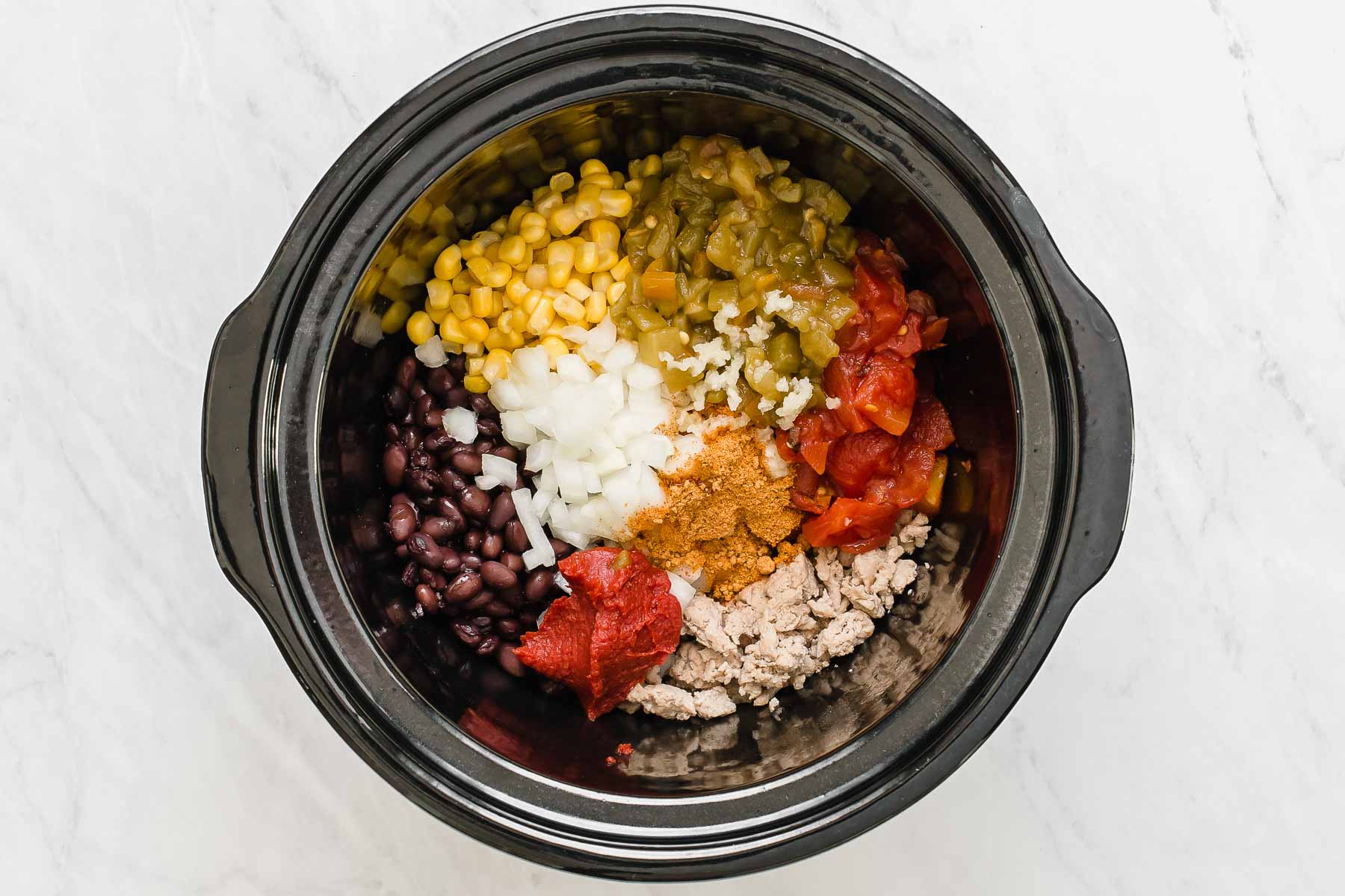 Individual ingredients for crockpot taco soup in black round slow cooker.