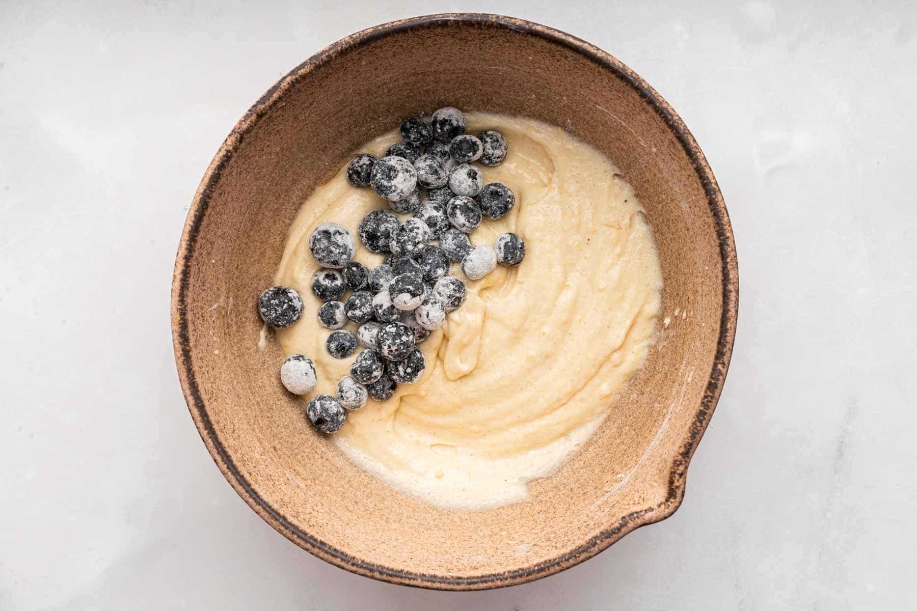 Fruit dusted with flour being stirred into cream colored batter.