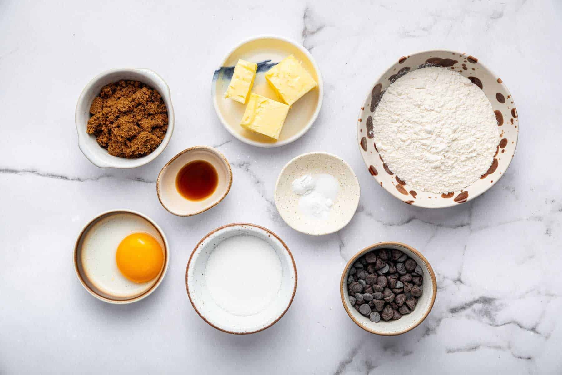 Small colorful bowls with brown sugar, egg yolk, chopped butter on counter.