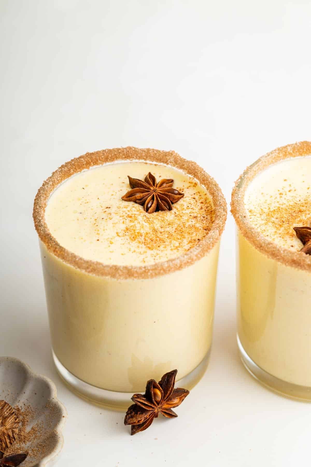 Side by side glasses of eggnog garnished with cinnamon, nutmeg and star anise.