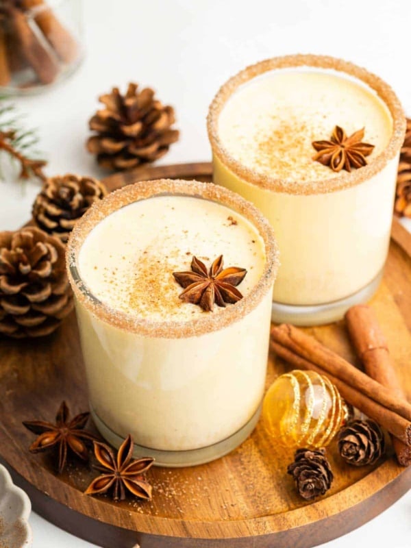 Two glasses of eggnog garnished with star anise and cinnamon sticks.