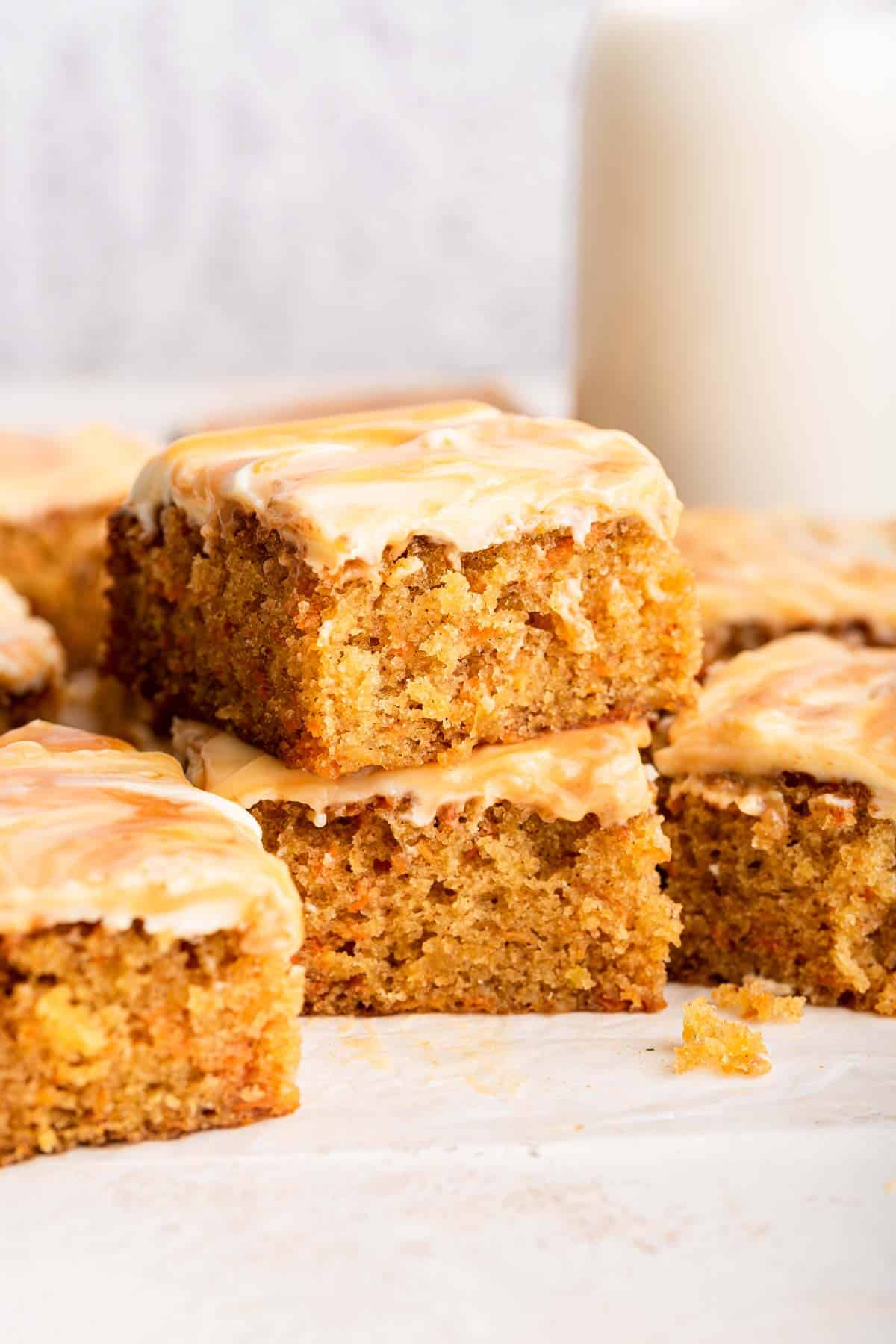 Two square pieces of carrot cake with caramel frosting stacked.