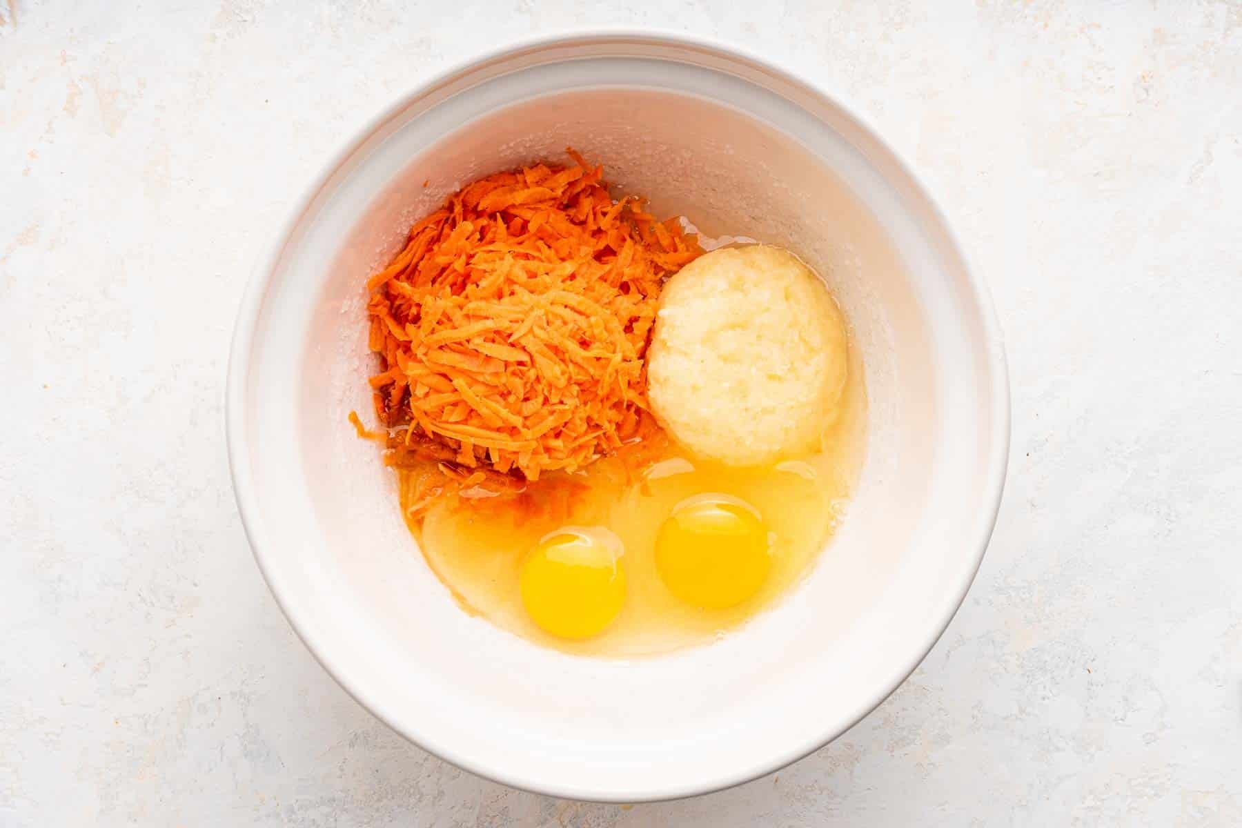 White bowl with grated carrots, pineapple and eggs.