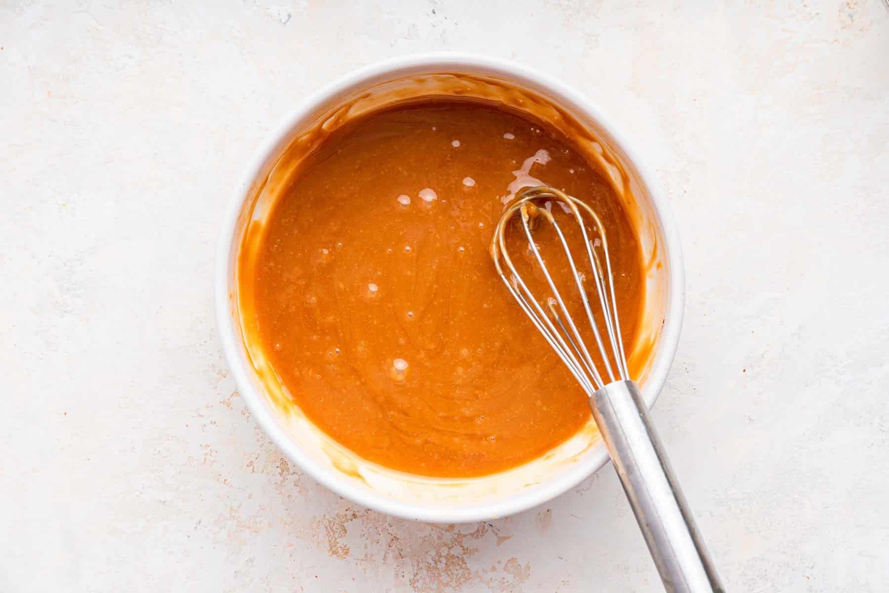 Bowl of melted caramel with a whisk.