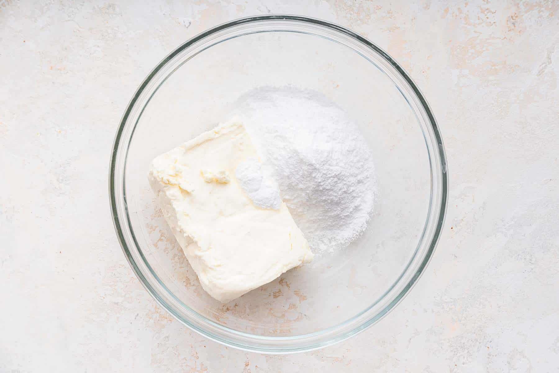 Clear bowl with cream cheese and powdered sugar.