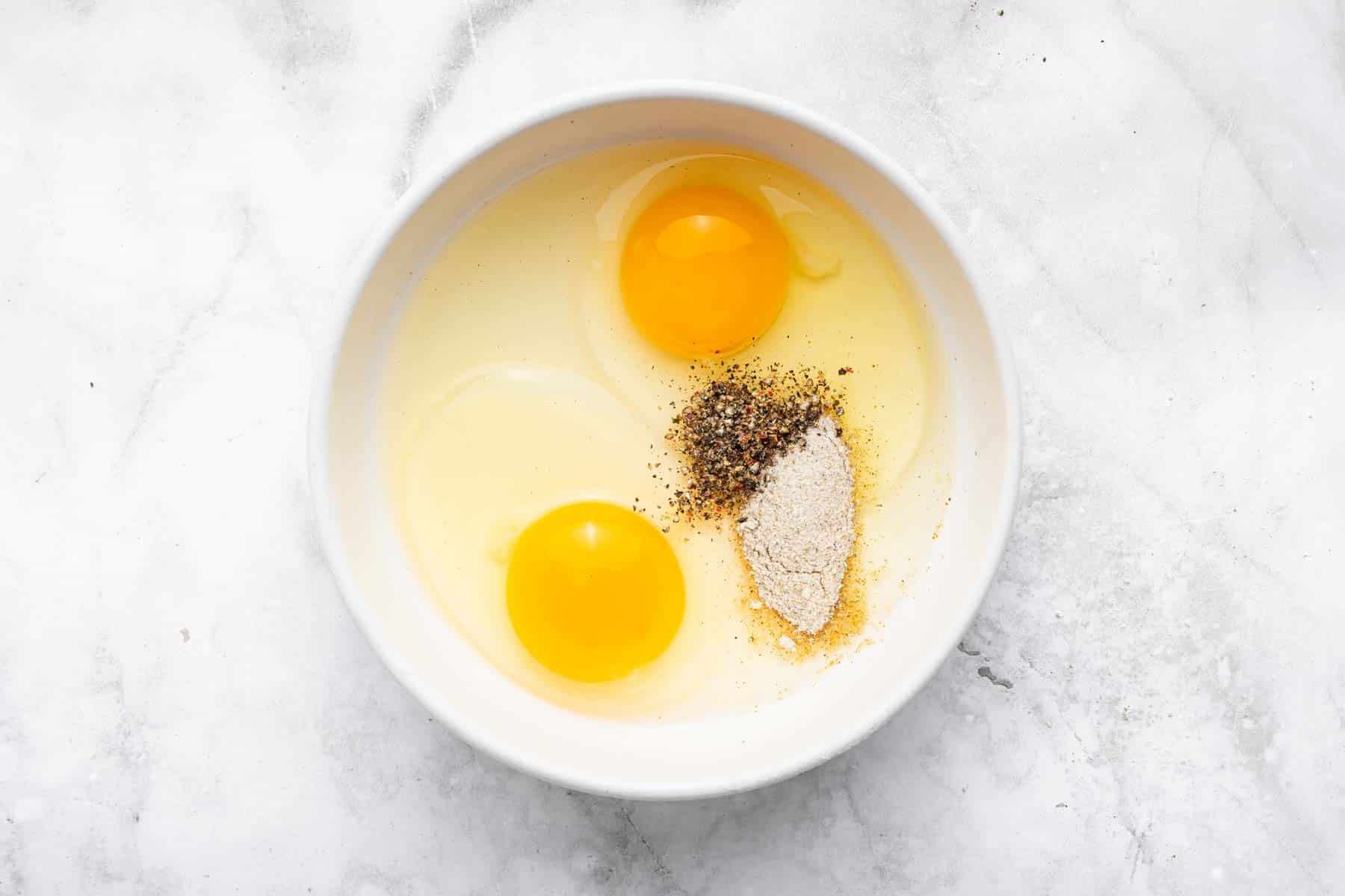 White bowl with two raw eggs, salt and pepper.