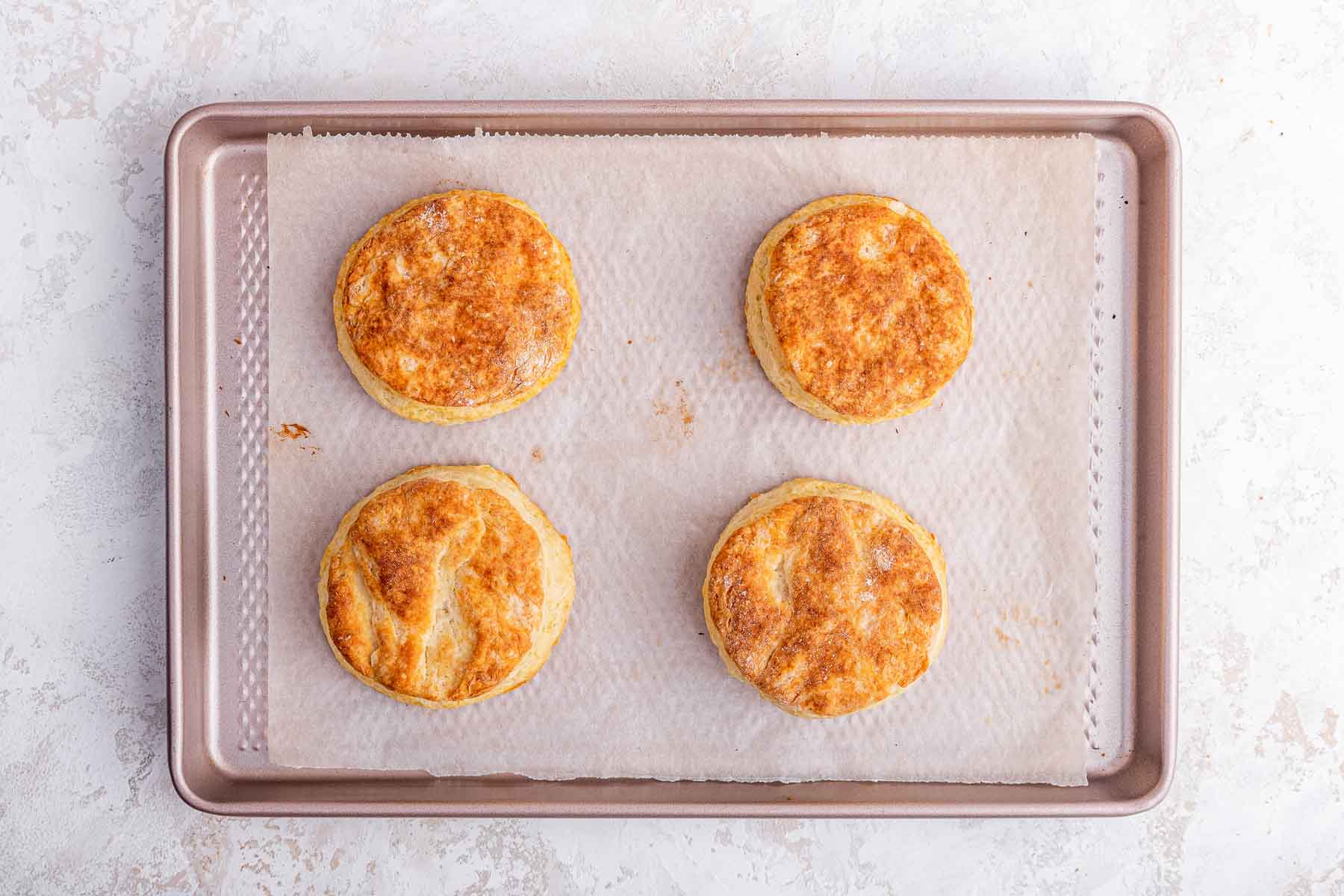 Four golden brown biscuits on baking sheet.