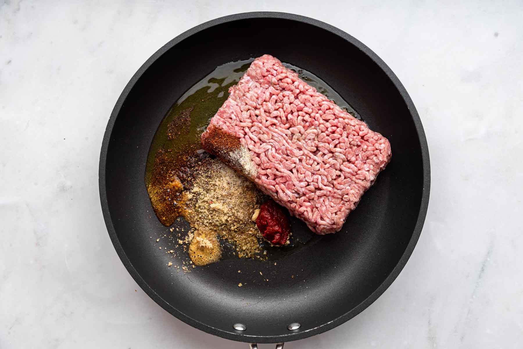 Pink meat in a black skillet with spices on the side.