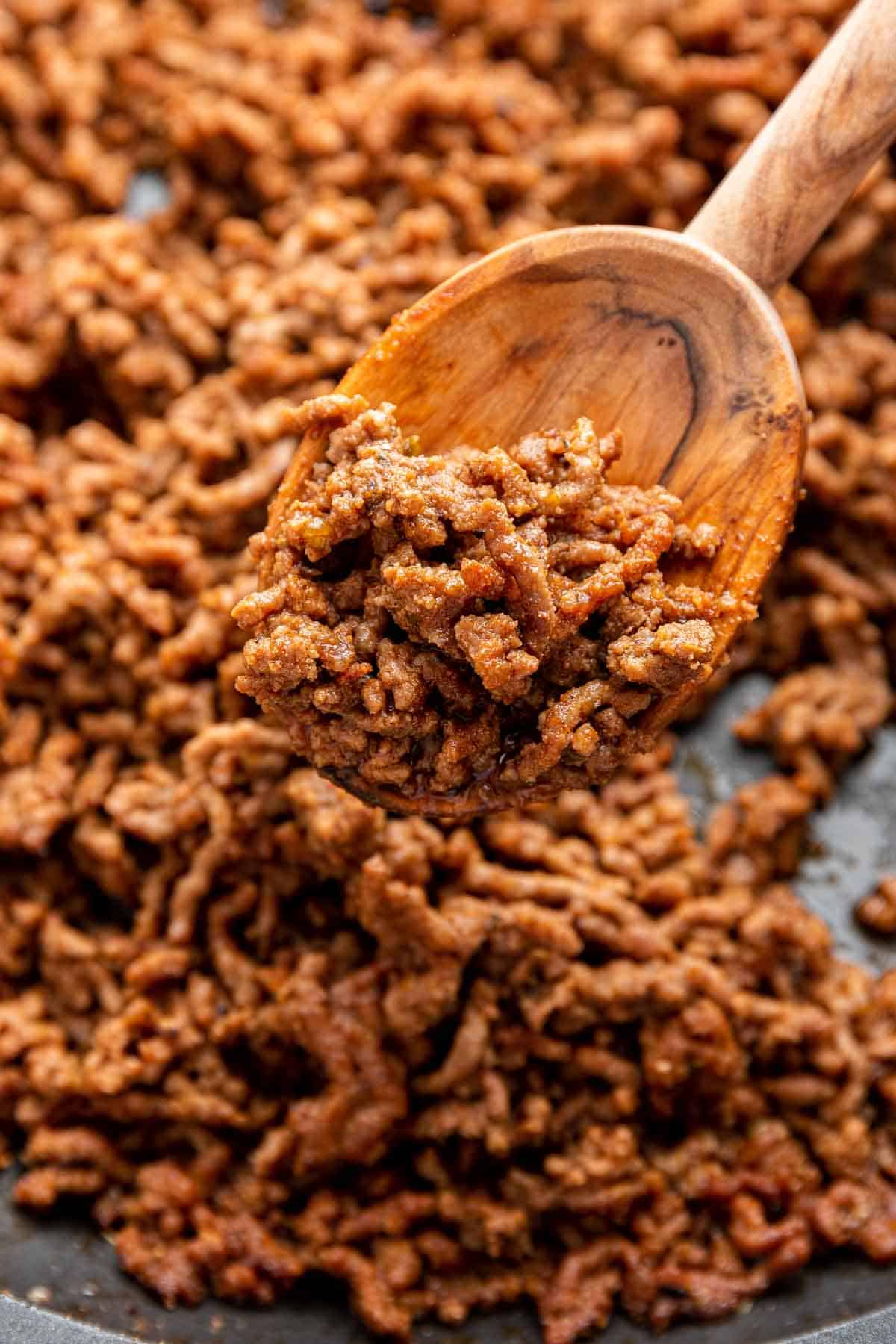 Brown taco meat in skillet with wooden spoon scooping it up.