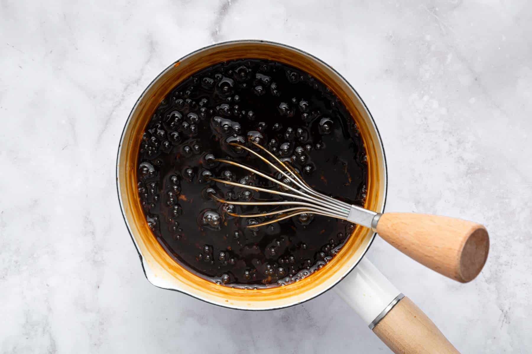 Brown syrup-like liquid in small white pot with whisk.