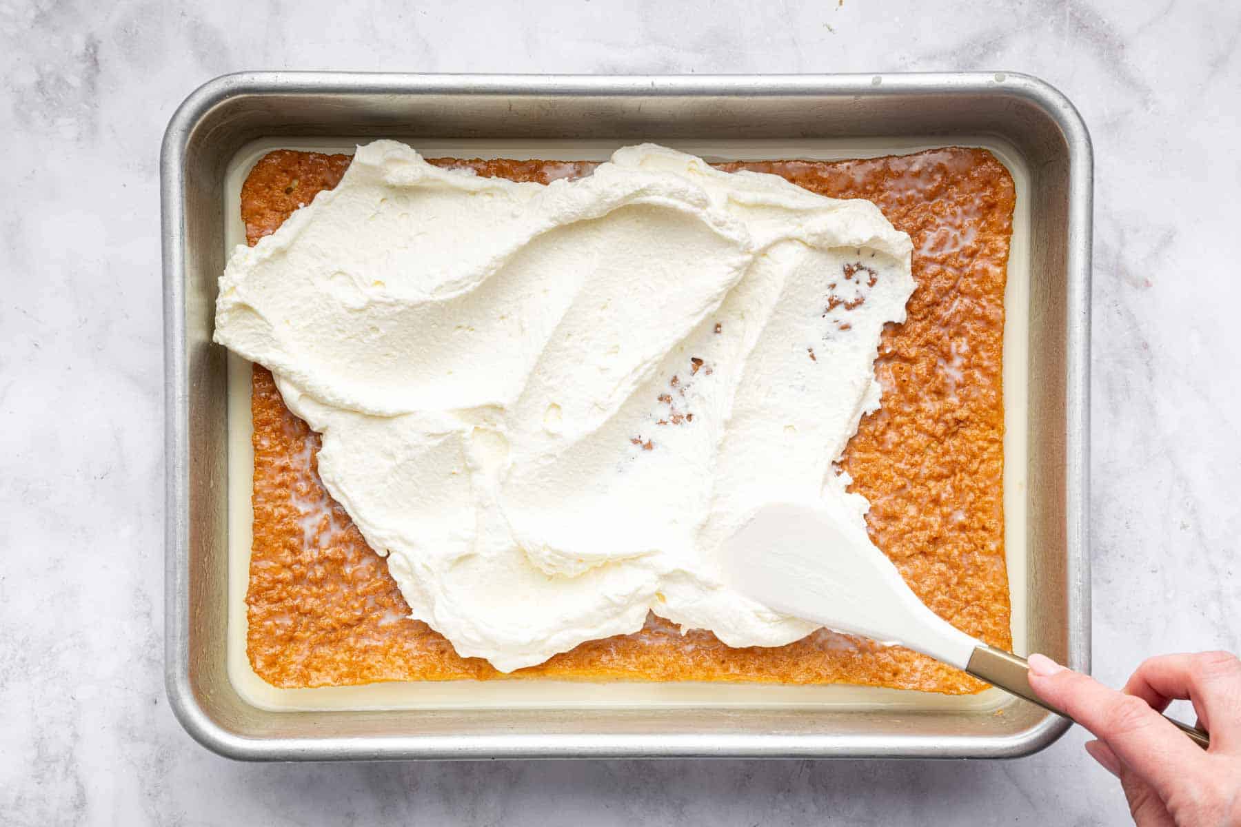 Spreading whipped frosting over rectangular sponge.