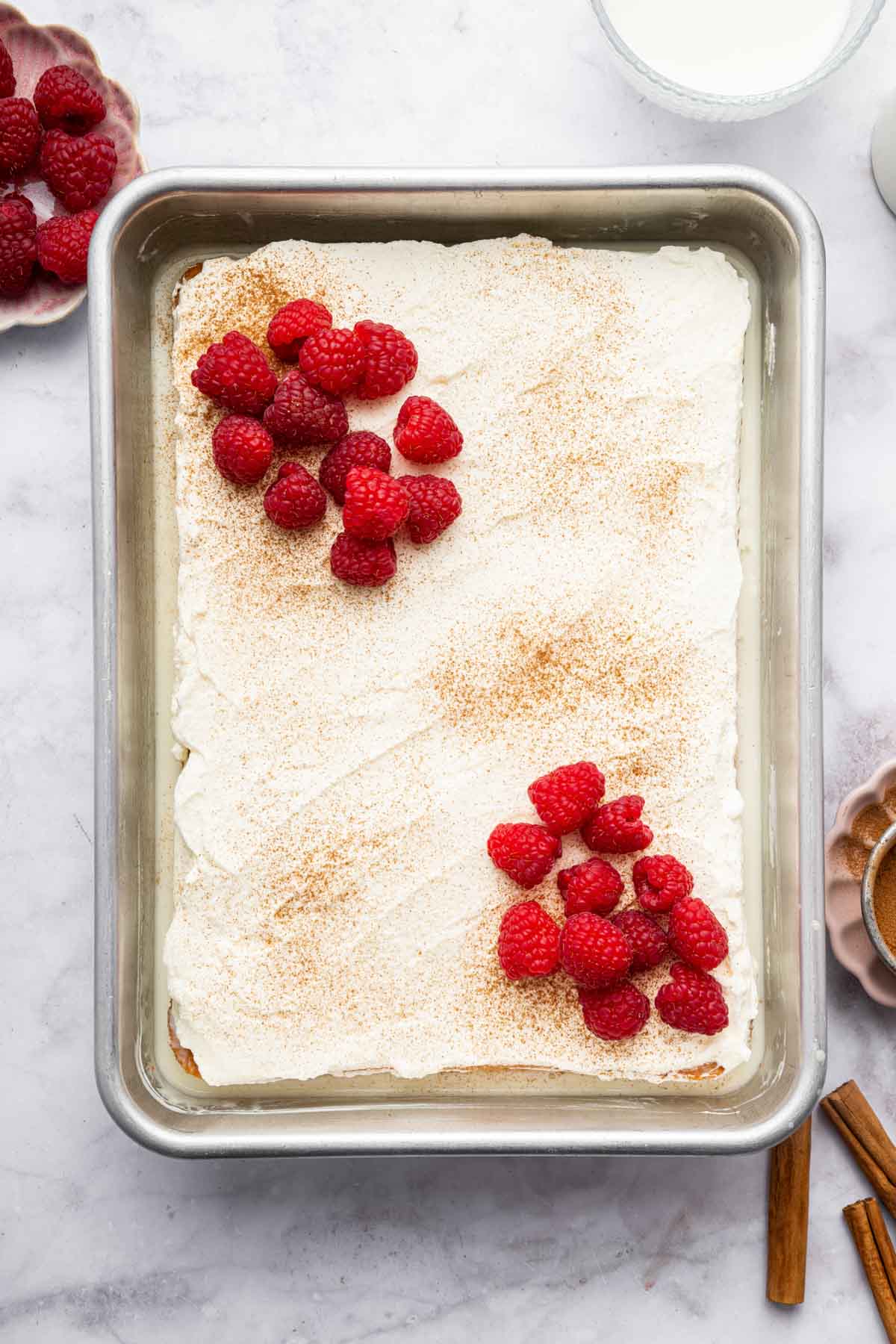 Vertical image of 9 x 13 tres leches cake garnished with raspberries and cinnamon.