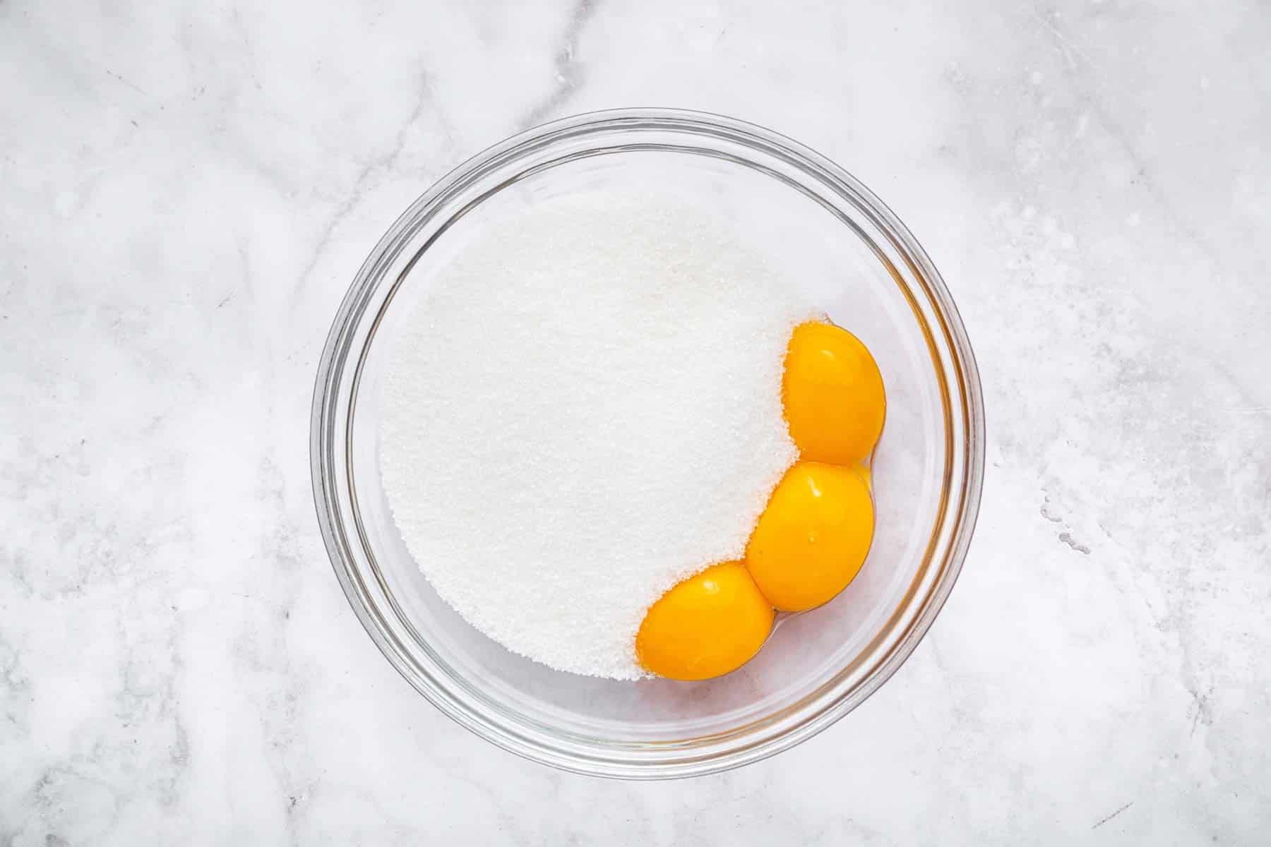 Clear bowl with sugar and egg yolks on the side.