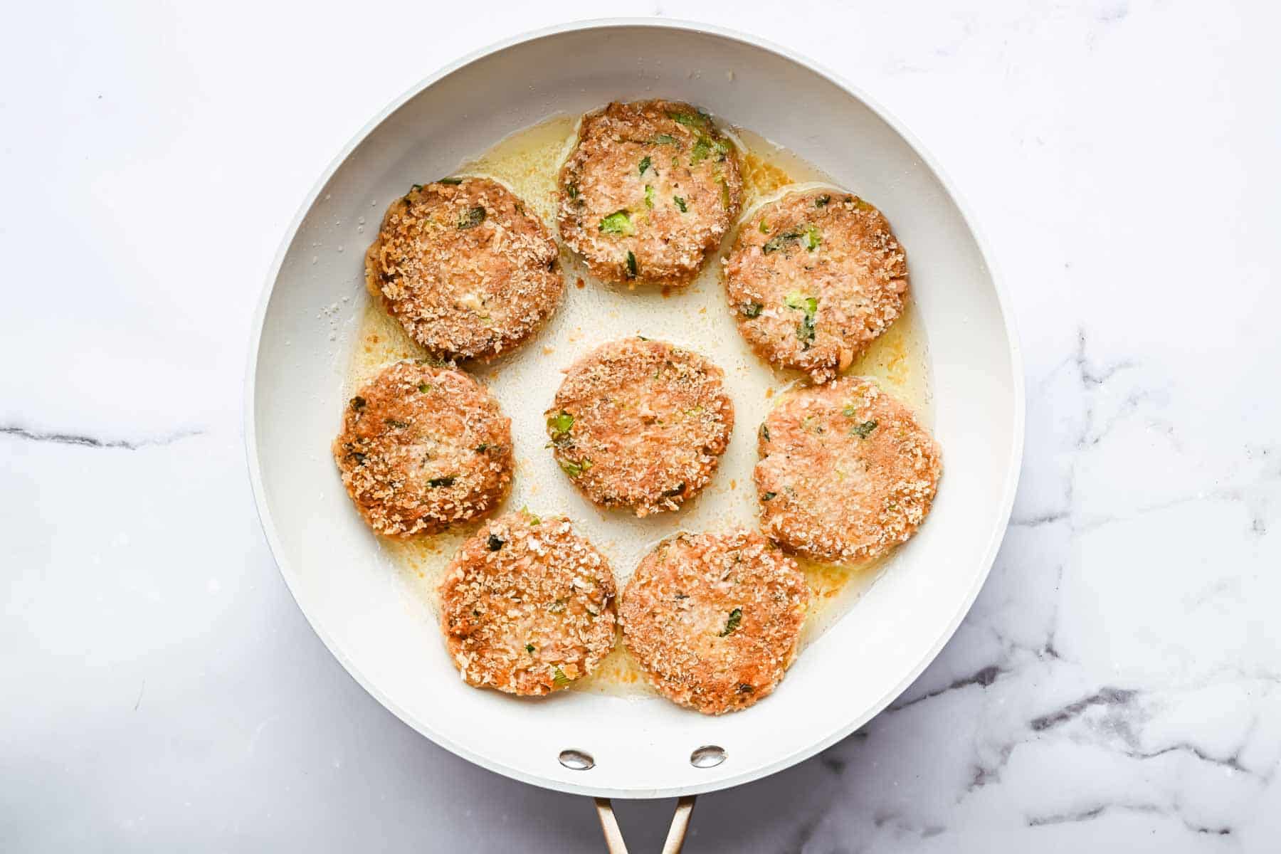 Round fritters being fried in a white pan.