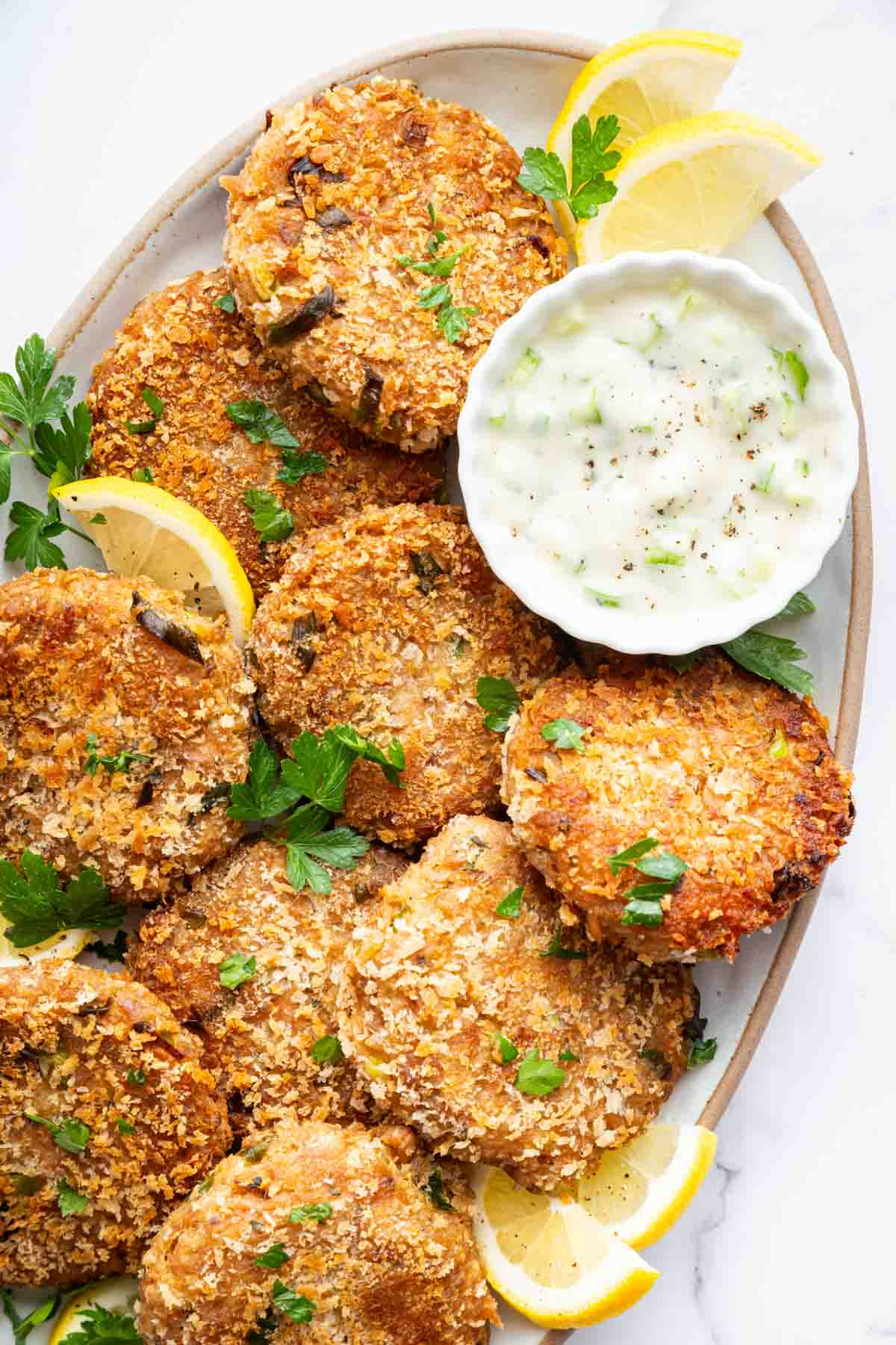 Vertical image of tuna patties on plate with bowl of ranch on the side.