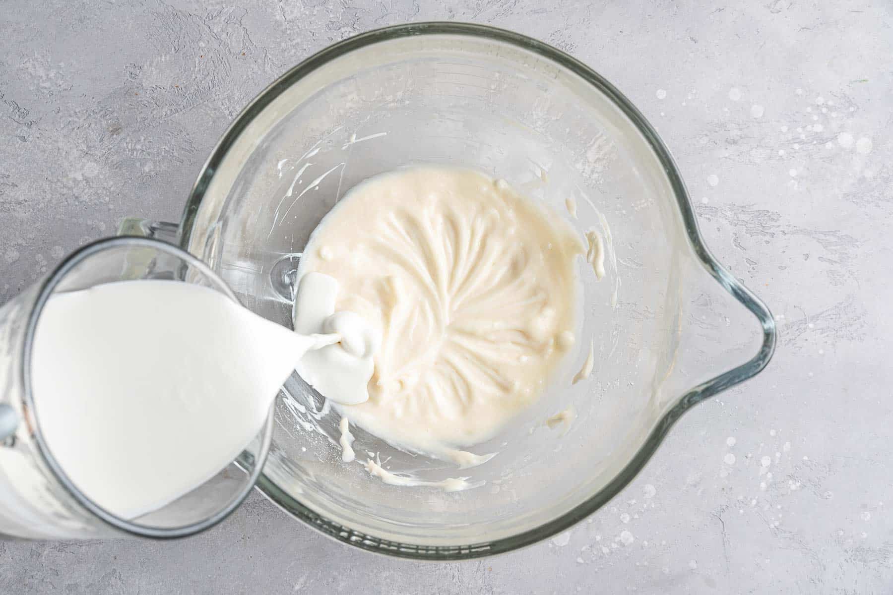Pouring heavy cream into cream cheese frosting.
