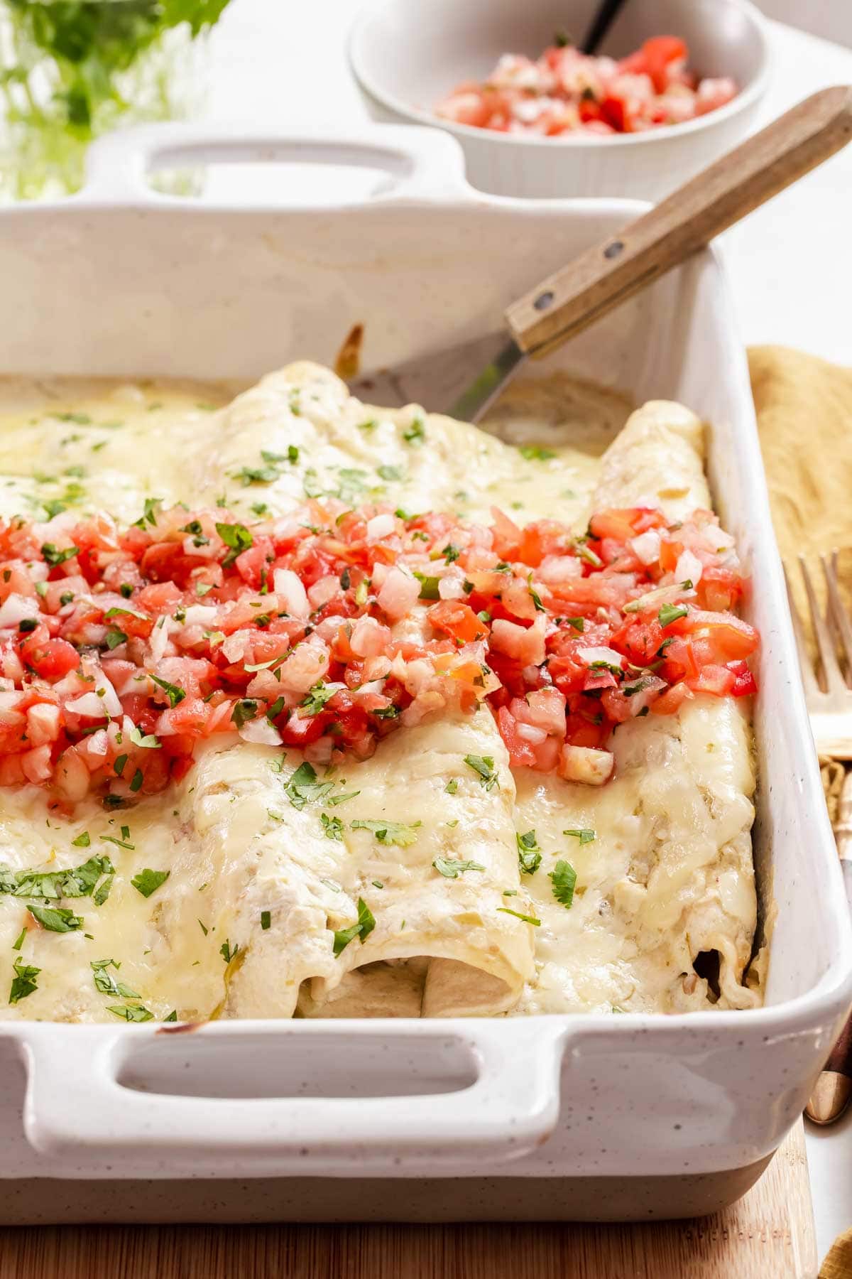 Pan of white chicken enchiladas with pico de gallo on top.