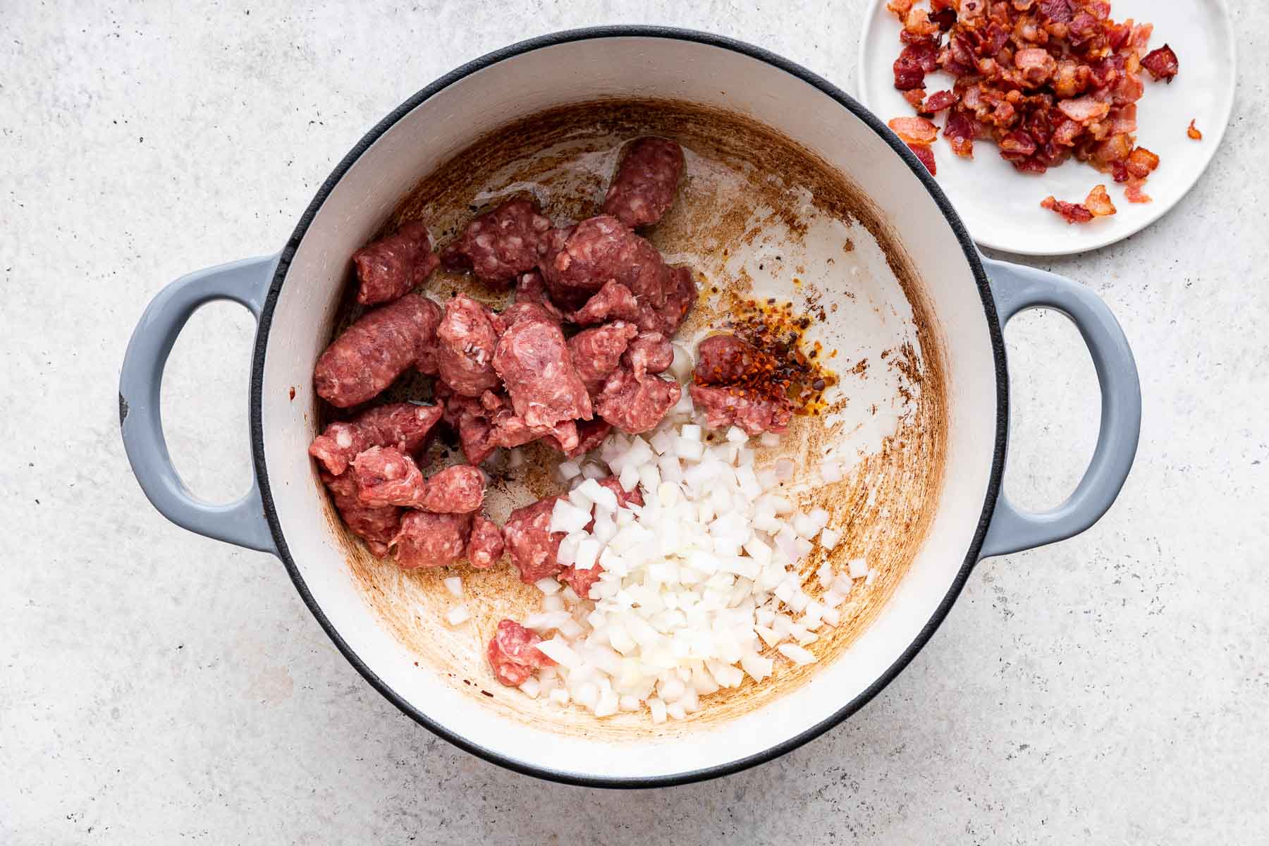 Raw sausage, onion and red pepper flakes in white pot.